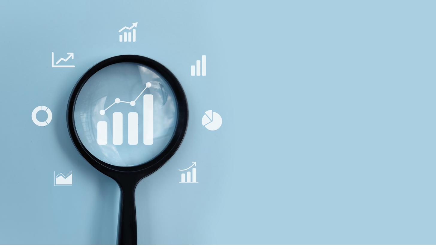 A magnifying glass held over rising bar charts and analytics icons